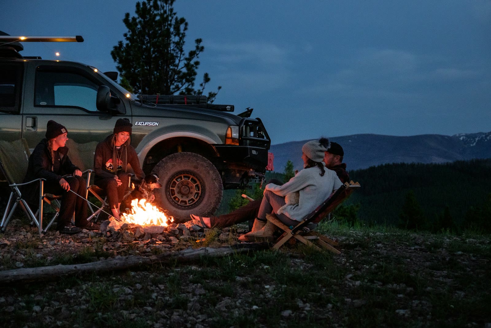 Camper sitting beside an SUV at a night trailhead campsite